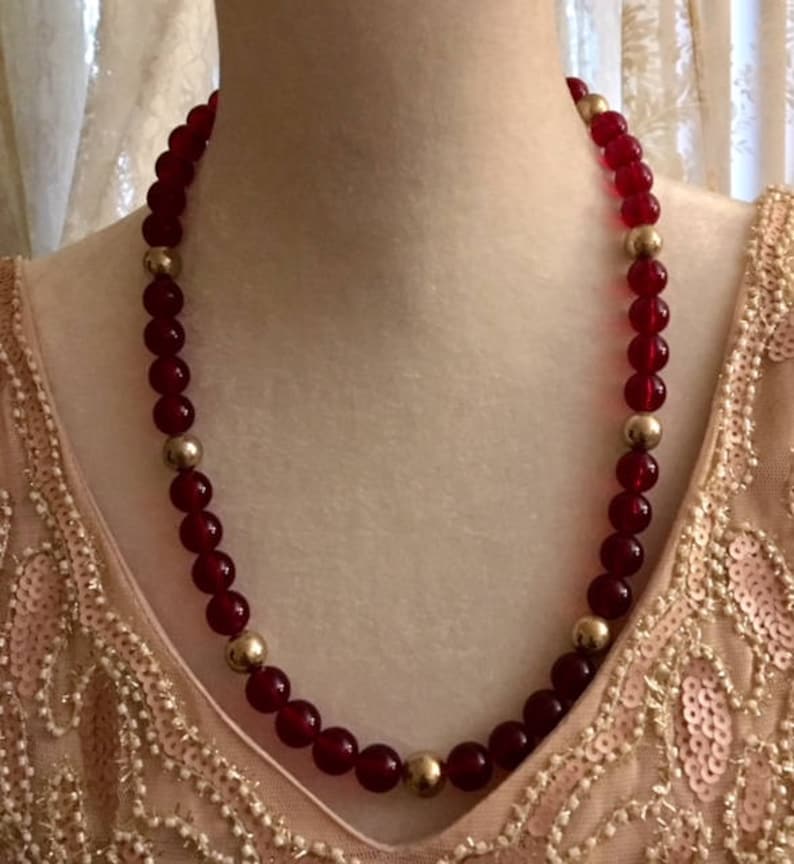 May include: A red and gold beaded necklace. The necklace is made of round, red glass beads with gold accents.