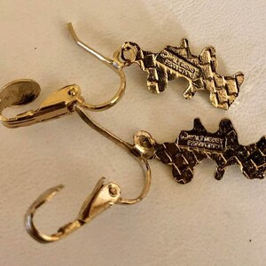 May include: A pair of gold-coloured earrings with a distinctive shape. The earrings feature a lever-back clasp and a textured pattern. The reverse of each earring is stamped with "&copy; WALT DISNEY PRODUCTIONS".