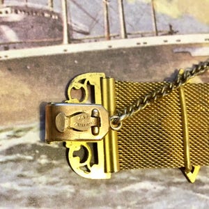 May include: Gold-toned metal mesh bracelet with a decorative clasp. The clasp has a filigree design and the words "Jae  Ancre" engraved on it.