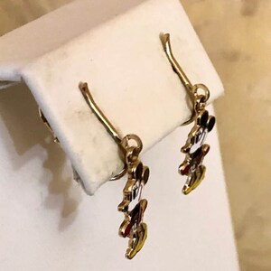 May include: Gold-coloured dangle earrings with a Mickey Mouse design. The earrings have a hook closure and feature Mickey's iconic face with black, white, red, and yellow enamel details. The earrings are displayed on a white surface.