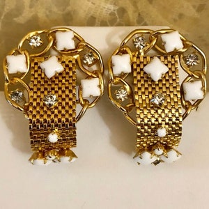 Puede incluir: Un par de pendientes de clip de tono dorado con esmalte blanco y diamantes de imitación transparentes. Los pendientes presentan un diseño de eslabón de cadena con forma rectangular.