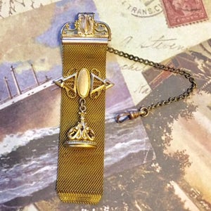 May include: A gold chain with a decorative fob. The fob is made of a mesh material and has a gold crown-shaped pendant. The chain is attached to a clasp.