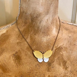 May include: A gold and silver butterfly pendant necklace. The butterfly pendant has a gold upper section and a silver lower section. The necklace is displayed on a mannequin with a gold-colored fabric.