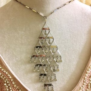 May include: A silver tone necklace with a geometric pendant featuring a cascading design of clear rhinestones.