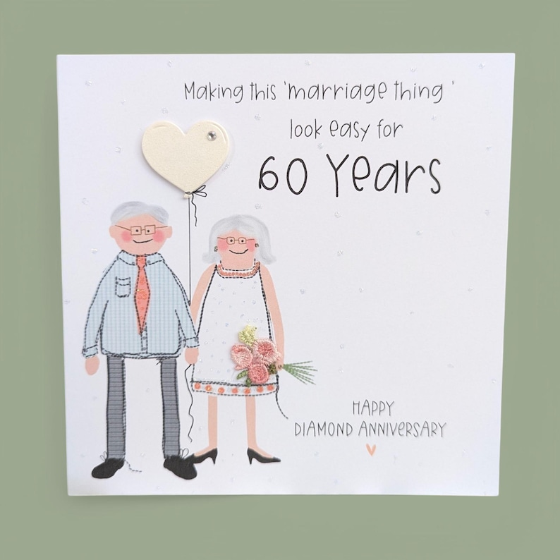 May include: A square greeting card featuring an illustration of an older couple. The text reads: Making this 'marriage thing' look easy for 60 Years. HAPPY DIAMOND ANNIVERSARY. The couple holds a cream heart balloon and a small bouquet of pink flowers.