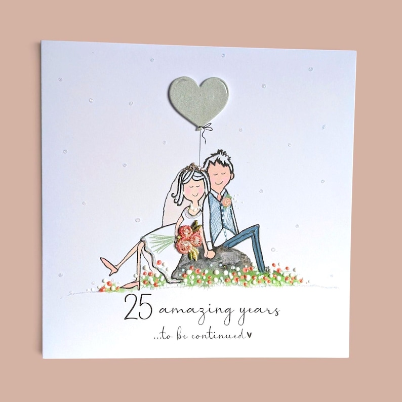 May include: A square greeting card featuring a hand-drawn illustration of a couple sitting on a rock, with a heart-shaped balloon above them. The text reads 25 amazing years ...to be continued. The design includes small floral accents and glitter.