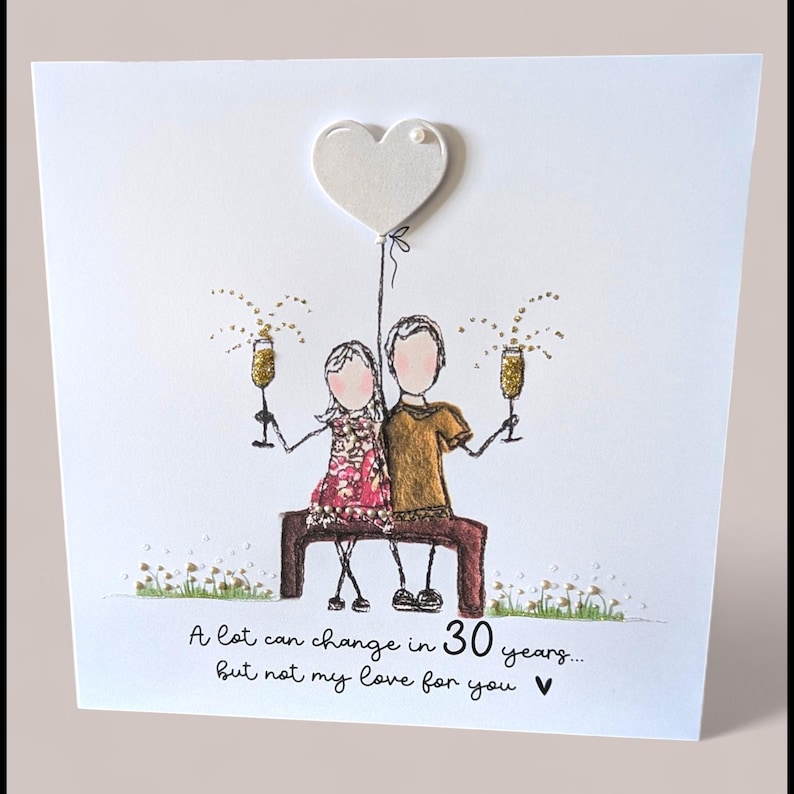 May include: A square greeting card featuring a line-art illustration of two figures sitting on a bench, holding gold glitter champagne flutes. Above them is a white heart balloon. The text reads: A lot can change in 30 years... but not my love for you.