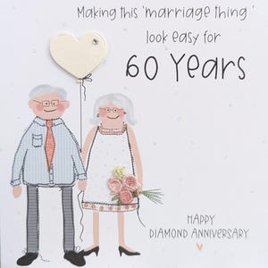 May include: A greeting card featuring an illustration of an older couple with gray hair and glasses. The text reads, Making this 'marriage thing' look easy for 60 Years, and Happy Diamond Anniversary. A cream heart balloon and pink flowers are included.