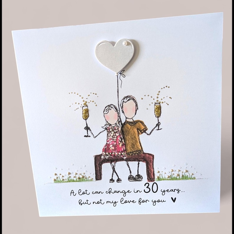 May include: A square greeting card featuring a hand-drawn illustration of two figures sitting on a bench, holding gold glitter champagne flutes. Above them is a white heart balloon. Text reads: A lot can change in 30 years... but not my love for you.