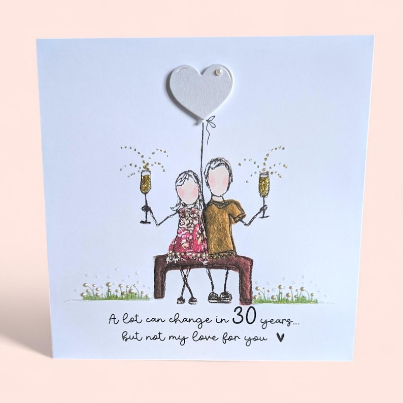 May include: A white greeting card featuring a hand-drawn illustration of two figures sitting on a brown bench, holding gold glitter champagne glasses. Above them is a white heart balloon. Text reads: A lot can change in 30 years... but not my love for you.
