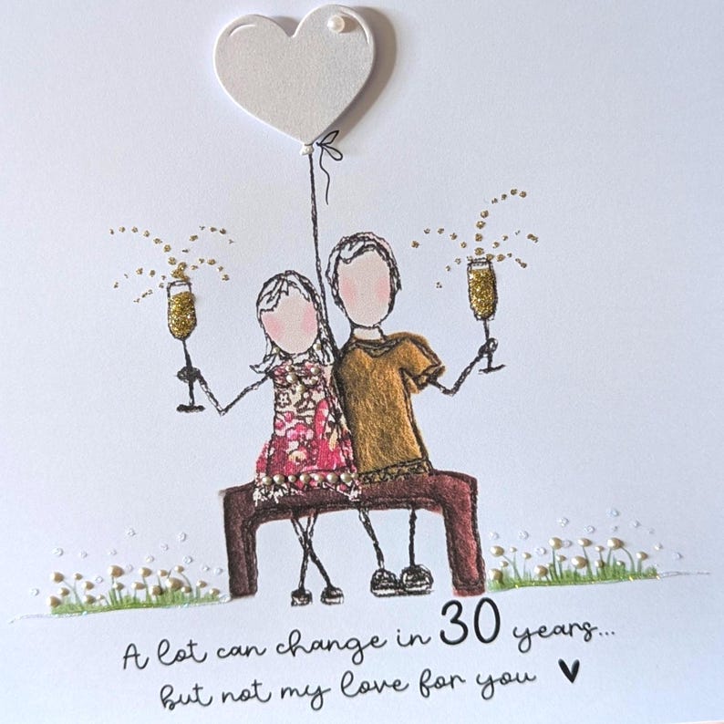 May include: A greeting card featuring a line-art illustration of two figures sitting on a bench, holding gold glitter champagne flutes. Above them is a white heart balloon. The text reads: A lot can change in 30 years... but not my love for you.