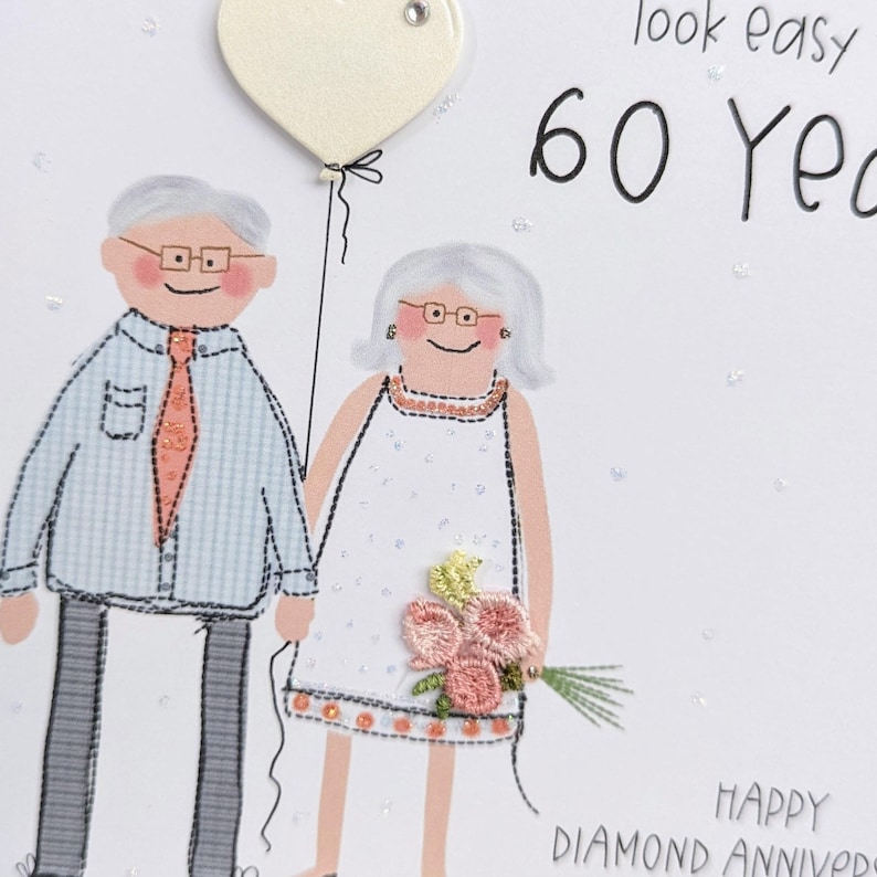 May include: A greeting card featuring an illustration of an older couple with gray hair and glasses. The person on the left wears a light blue shirt and orange tie, while the person on the right wears a white dress with pink floral embroidery.