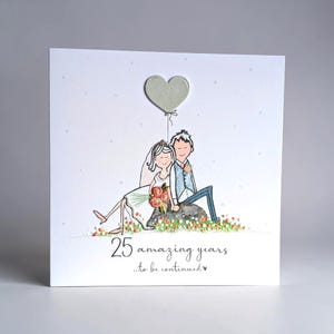May include: A square greeting card featuring a hand-drawn illustration of a couple sitting on a rock, with a heart-shaped balloon above them. The text reads 25 amazing years ...to be continued. The design includes small colourful floral accents.