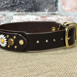 以下が含まれることがあります： 真鍮のバックルと装飾的な花のアクセントが付いた、茶色の革製の犬用首輪です。