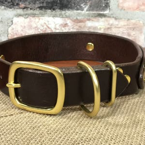 以下が含まれることがあります： 真鍮製の金具が付いた茶色の革製の犬用首輪。バックル、Dリング2つ、装飾的なスタッドが付いています。