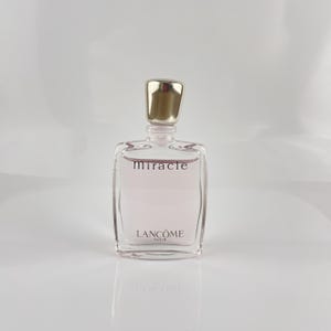 Könnte beinhalten: Ein klarer, rechteckiger Parfümflakon mit goldenem Verschluss. Die Flasche enthält eine hellrosa Flüssigkeit und trägt das Wort "miracle" und den Markennamen "Lancôme" in schwarzer Schrift. Der Flakon steht auf einer weißen Oberfläche.