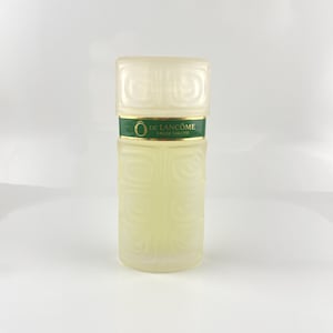 Puede incluir: Un frasco de perfume de vidrio esmerilado con un líquido amarillo claro en su interior. El frasco tiene una tapa blanca y una banda verde con la inscripción dorada "DE LANCÔME EAU DE TOILETTE". El frasco tiene un diseño texturizado.