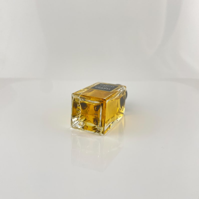 May include: A rectangular perfume bottle with a black label that reads "COCO CHANEL". The bottle is filled with a golden-colored liquid. The bottle is made of clear glass and has a black cap.