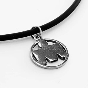 May include: A black rubber necklace with a silver pendant featuring a stylized bird design.