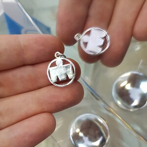May include: Two silver charms in the shape of a running person, a popular symbol for marathon runners. The charms are round and have a smooth, polished finish.