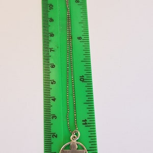 May include: A silver chain necklace with a silver pendant featuring a stylized human figure inside a circle. The pendant is about 1 inch in diameter.