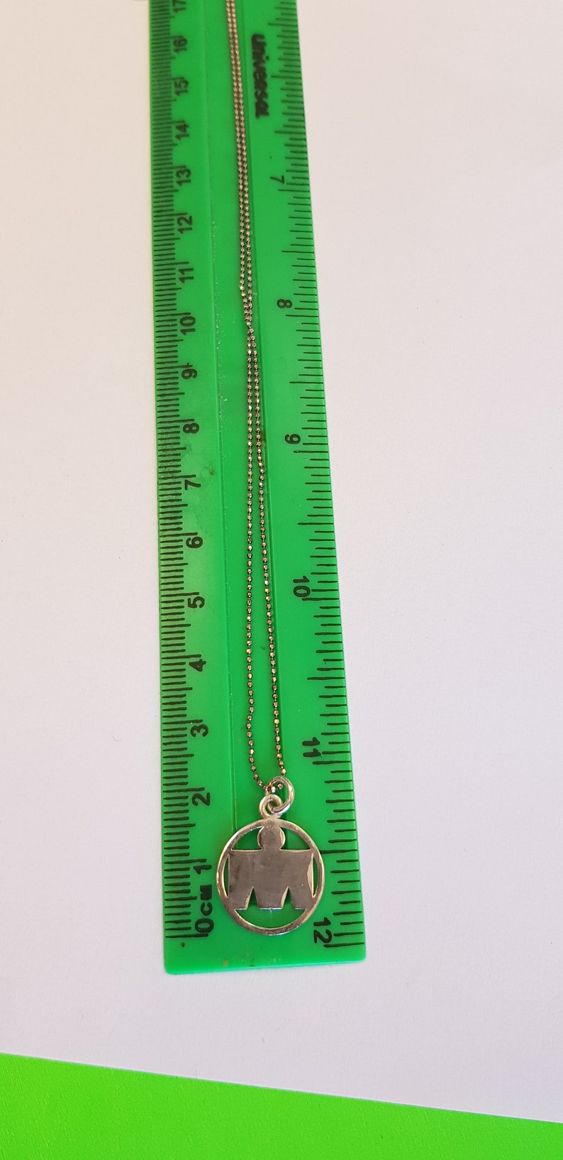 May include: A silver chain necklace with a silver pendant featuring a stylized human figure inside a circle. The pendant is about 1 inch in diameter.