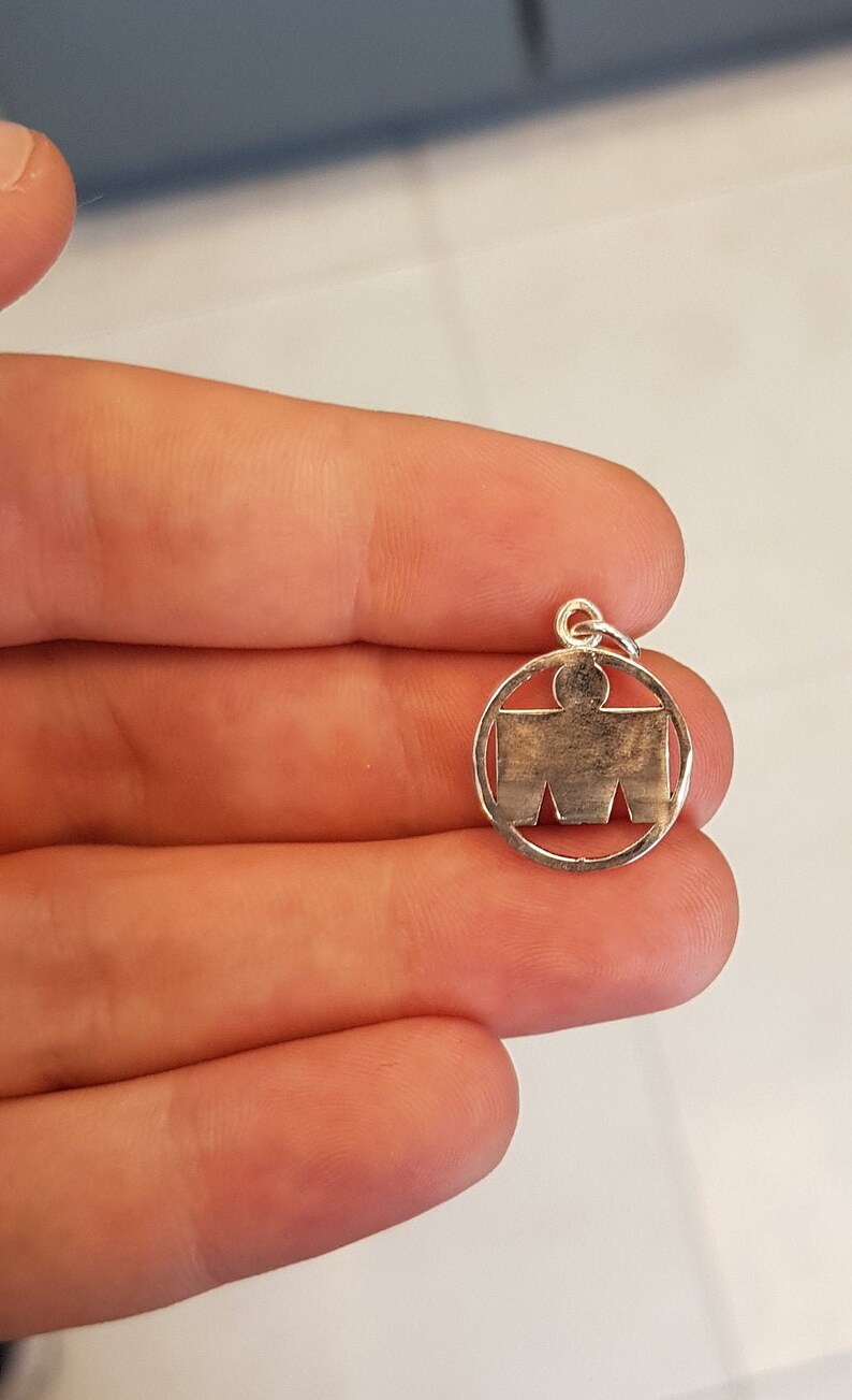 May include: Silver charm with a stylized human figure inside a circle.