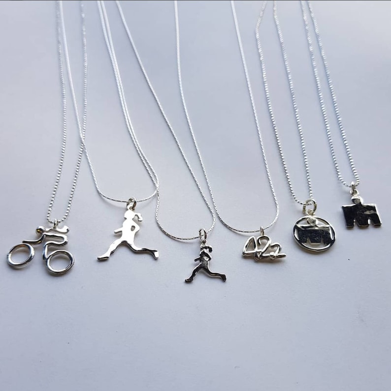 May include: Six silver necklaces with different charms, including a bicycle, a runner, a number "42.2", a marathon runner, and a marathon symbol.