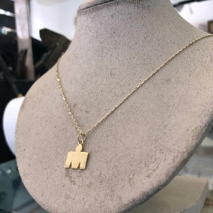 May include: A gold chain necklace with a gold pendant shaped like a person. The pendant is a simple silhouette of a person with arms outstretched.