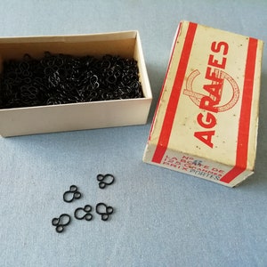 Peut inclure: Une boîte blanche remplie d'agrafes métalliques noires, étiquetée "AGRAFEES" avec le texte "LA BOITE DE 125 GRAMMES PRIX PORTES" sur le côté.