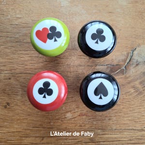 Peut inclure: Quatre boutons ronds avec un cercle blanc au centre et un symbole de carte à jouer noir. Les boutons sont vert, noir, rouge et noir. Les symboles sont un cœur, un trèfle, un trèfle et une pique.