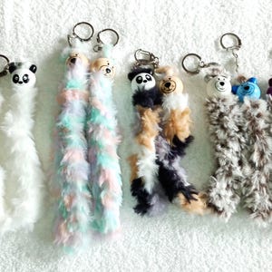 Pode incluir: Seis chaveiros fofinhos e coloridos com diferentes rostos de animais. Os chaveiros são feitos de um material macio e felpudo e apresentam uma variedade de cores, incluindo branco, rosa, azul, verde, marrom e preto. Cada chaveiro tem um anel de metal para prender em chaves ou bolsas.