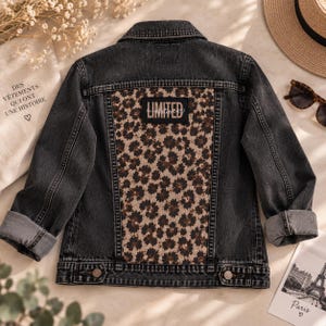 Könnte beinhalten: Eine anthrazitfarbene Jeansjacke mit einem großen Rückenteil in braun-schwarzem Leopardenmuster. Ein schwarzer rechteckiger Aufnäher ist mittig auf dem Rückenteil platziert, mit dem weißen Schriftzug LIMITED EDITION in Schreibschrift.