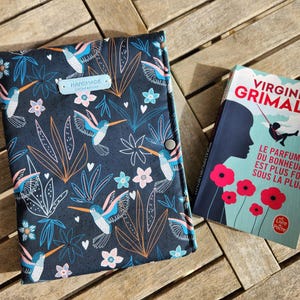 Może przedstawiać: Ciemnoniebieska okładka książki z wzorem kolibrów i kwiatów obok książki zatytułowanej "Virginie Grimaldi". Okładka książki ma sylwetkę osoby i tekst "Le Parfum du Bonheur est plus fort sous la pluie".
