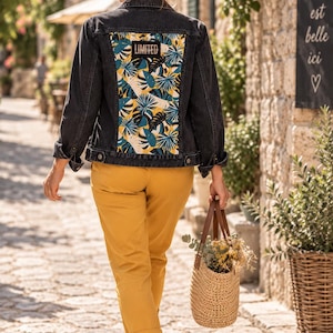Pode incluir: Um casaco de ganga preto com um grande painel traseiro retangular com uma estampa de folhas tropicais em tons de azul, amarelo e branco, e um emblema preto com a palavra LIMITED em branco, combinado com calças amarelo mostarda.