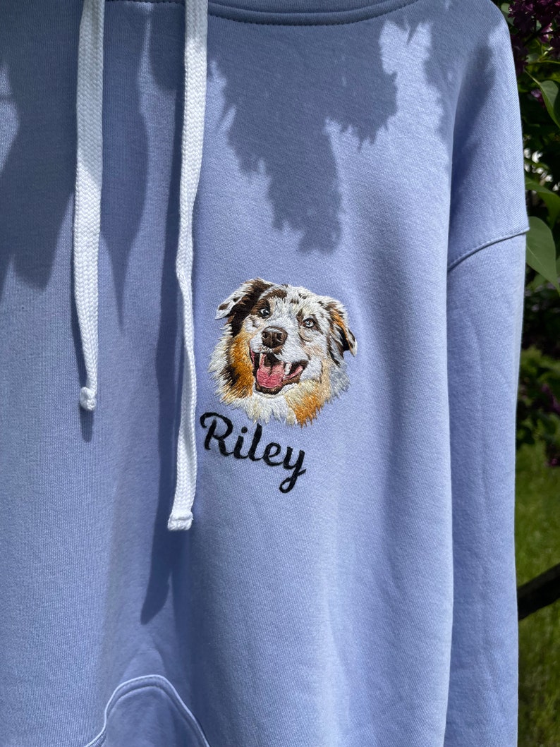 May include: A light blue hoodie with a white drawstring. The hoodie features an embroidered image of a dog's head with the name "Riley" underneath.