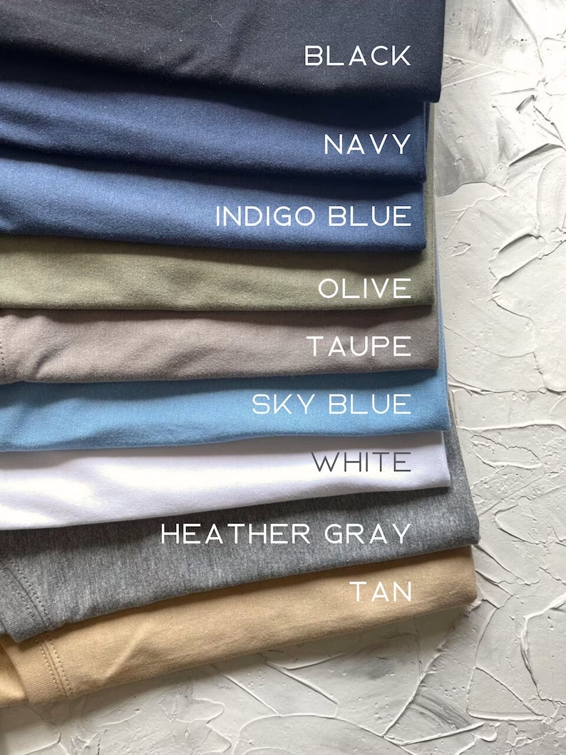May include: A stack of t-shirts in various colors, including black, navy, indigo blue, olive, taupe, sky blue, white, heather gray, and tan.