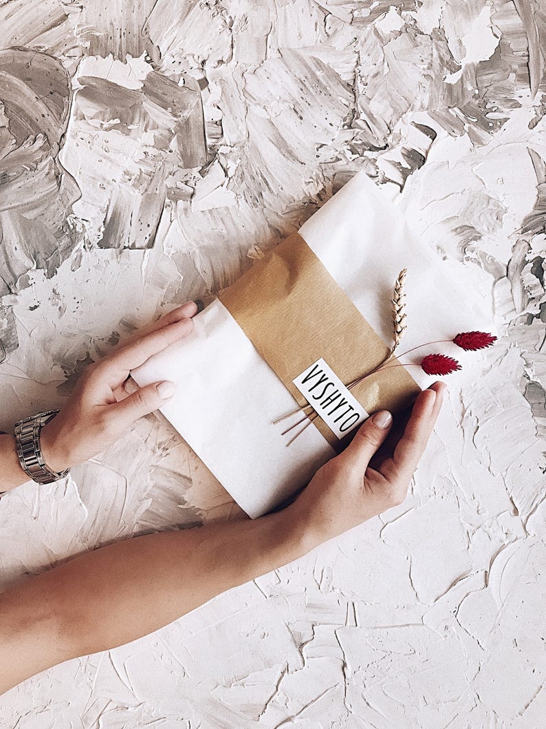 May include: A brown paper package wrapped in white tissue paper with a small sprig of wheat and red dried flowers. The package is labeled with the word "VYSHYTO" in black lettering.