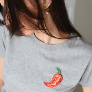 May include: A grey t-shirt with an embroidered red chilli pepper on the front.