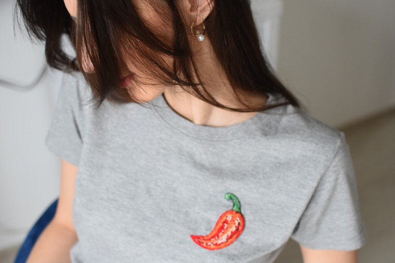 May include: A grey t-shirt with an embroidered red chilli pepper on the front.