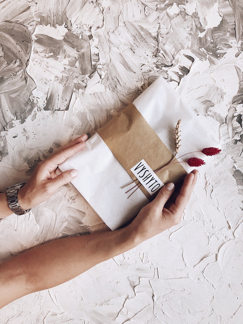 May include: A white gift bag with a brown paper strip and a small white label with the text "VYSHYTO" on it. The bag is decorated with dried wheat stalks and red flowers.