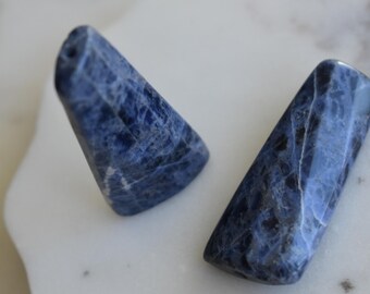 May include: Two blue and white, smooth, polished, natural stone, gemstone, or crystal,  cabochons. The stones are in the shape of a triangle and a rectangle.