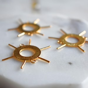 Könnte beinhalten: Drei goldfarbene Metall-Sonnenanhänger mit einem runden Zentrum und sechs strahlenden Punkten. Die Anhänger haben eine strukturierte Oberfläche und sind perfekt für die Schmuckherstellung.