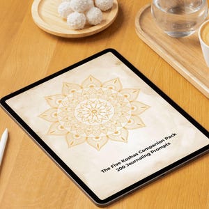 Puede incluir: Una tableta que muestra un documento digital con una ilustración de mandala dorada sobre un fondo beige claro. El texto en la pantalla dice The Five Koshas Companion Pack 200 Journaling Prompts. Un lápiz óptico blanco está junto a la tableta.