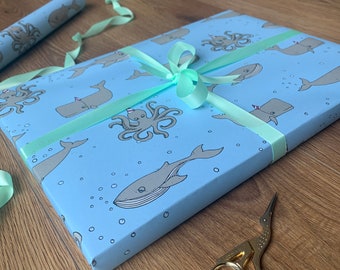 May include: Blue wrapping paper with a pattern of whales, octopuses, and bubbles. A green ribbon is tied around the paper.