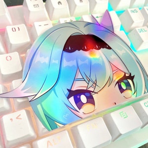 May include: A holographic sticker of a cartoon girl with blue hair and large eyes. The sticker is placed on a white keyboard with pink and blue accents.