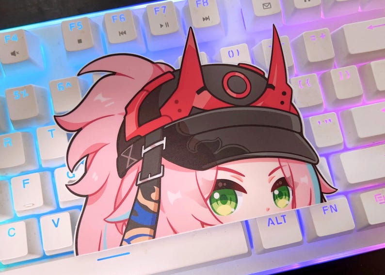 May include: A sticker featuring a cartoon character with pink hair and green eyes, wearing a red and black headpiece. The sticker is placed on a white keyboard with blue and purple backlighting. The sticker is partially covering the ALT key.
