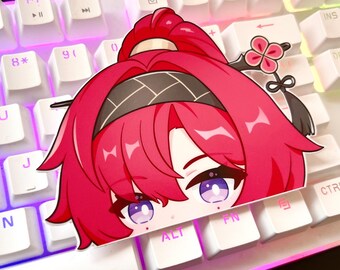 Puede incluir: Una pegatina con un personaje de anime de dibujos animados con cabello rosado, una diadema negra y ojos grandes de color morado. El personaje está mirando por encima de la parte superior de un teclado blanco.