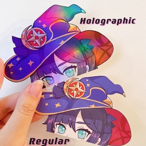 May include: Two stickers featuring a cartoon character with a witch hat. One is holographic with a rainbow gradient, the other is regular. The hats are dark blue with gold stars and a crescent moon. Text on the stickers reads "Holographic" and "Regular".