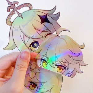 May include: Three iridescent holographic stickers featuring anime-style characters with blonde hair. The characters have large eyes and are smiling. The stickers are cut out and have a glossy finish.
